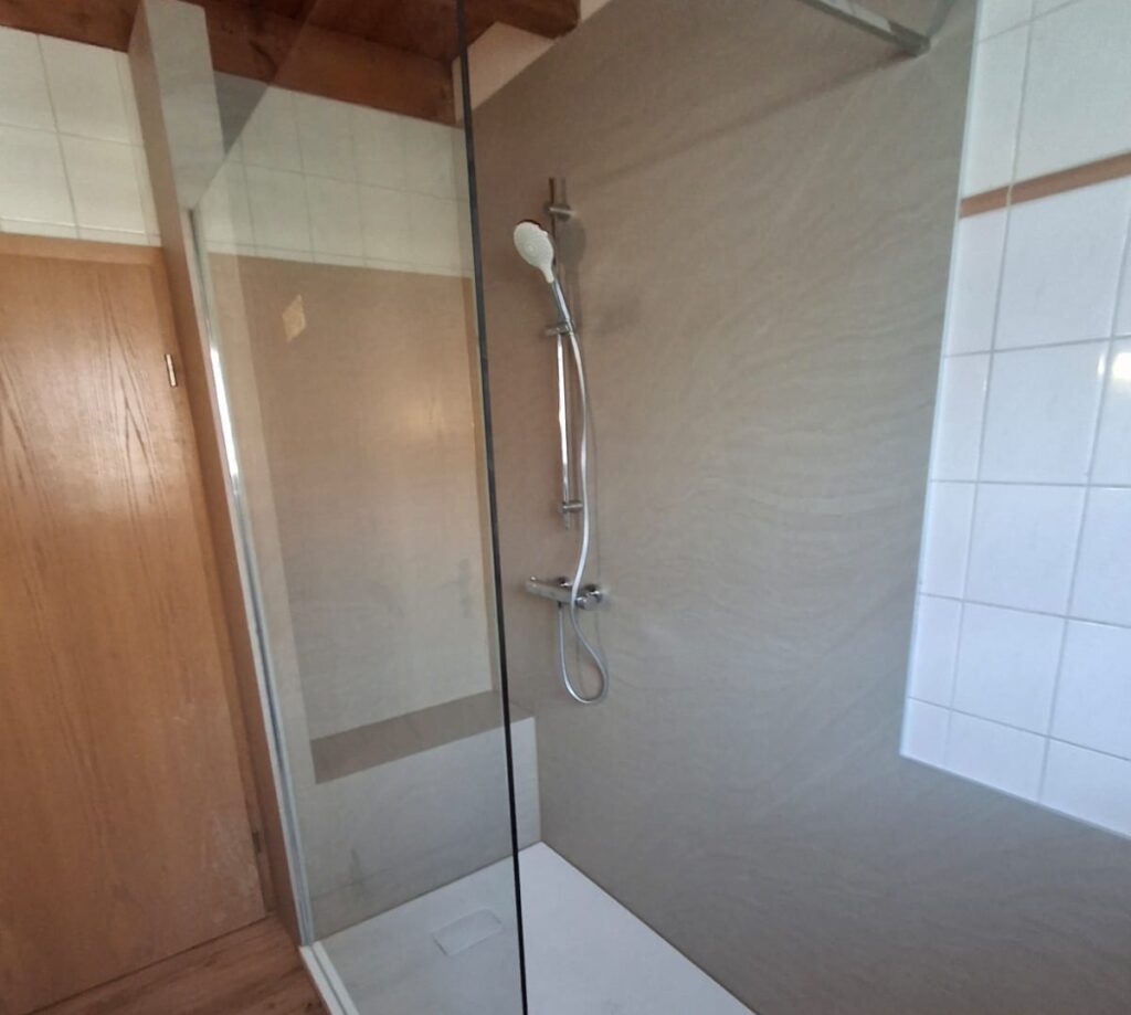 Barrierearme Dusche mit Duschwand aus Glas und niedriger Duschwanne mit fugenlosen grauen Platten
